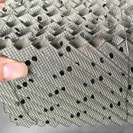 A hand is holding a piece of perforated plate structured packing.